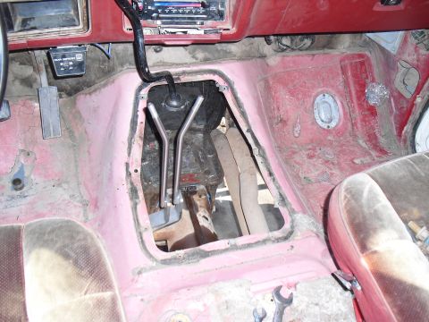 1986 Ford Bronco - The interior floor of a vehicle shows exposed mechanical components and worn upholstery, with a watermark at the bottom right.