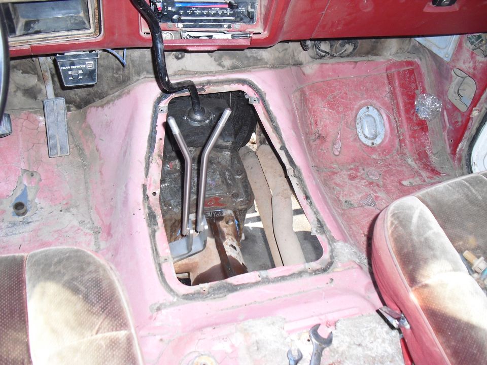 Interior floor of a vehicle with exposed transmission tunnel and worn seats. A "Supermotors.net" watermark is visible