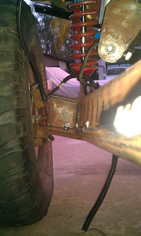 1992 Ford Ranger - Close-up of a modified truck's suspension system, showing a red coilover shock and a large tire with visible rust on the frame.