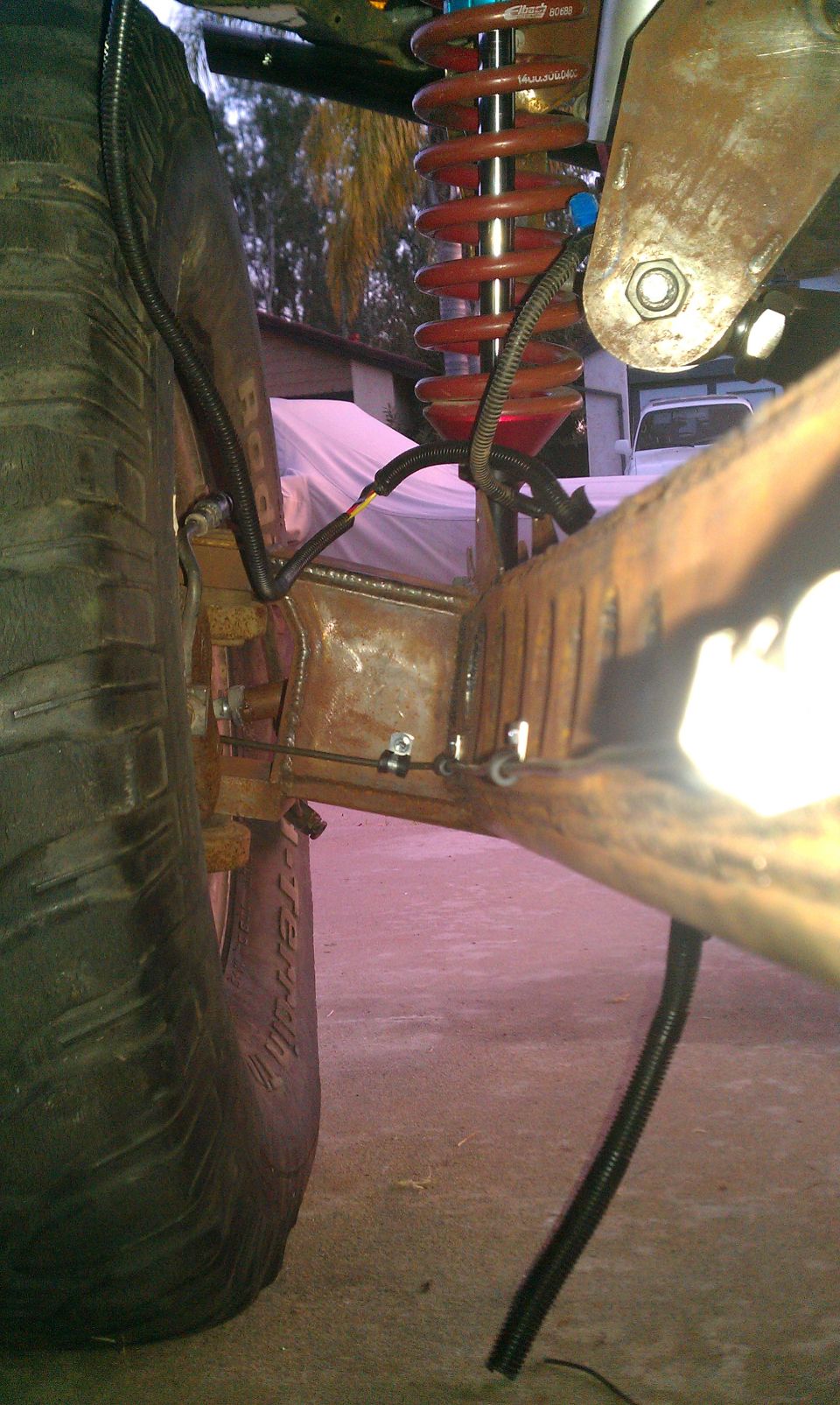 Truck suspension with red coilover shock and large tire. Rusty metal frame visible