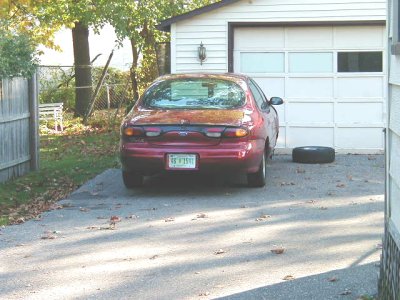 1997 Ford Taurus - Rear view of a 1997 Ford Taurus parked in a driveway next to a garage with a spare tire nearby.