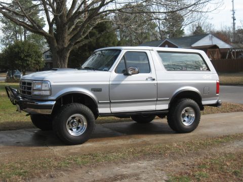 1994 Ford Bronco - Silver and white Ford Bronco with aftermarket bumper and lifted suspension, viewed from the front three-quarter angle.