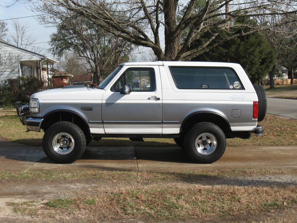 Side view of a white and silver 1994 Ford Bronco with a spare tire on the back