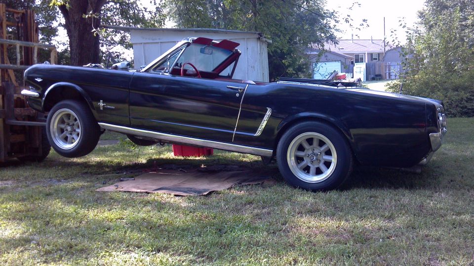 Black convertible Mustang lifted by a forklift, showing a red oil pan underneath.