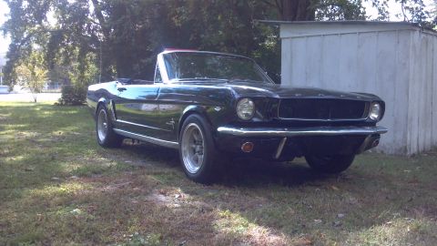 1965 Ford Mustang - A classic black 1965 Ford Mustang convertible sits in a grassy yard next to a white shed.