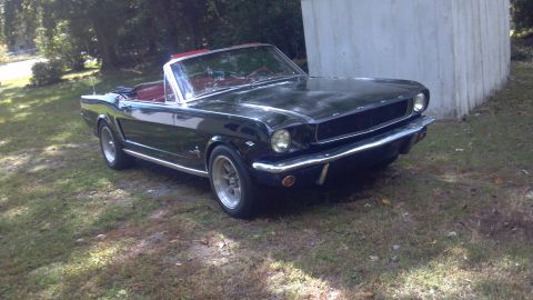 1965 Ford Mustang - A black 1965 Ford Mustang convertible sits on a grassy area next to a concrete structure.