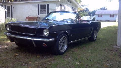 1965 Ford Mustang - A classic black 1965 Ford Mustang convertible sits in a residential yard on a sunny day.