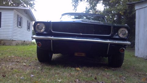 1965 Ford Mustang - Front view of a black 1965 Ford Mustang convertible parked in a grassy yard next to a house.