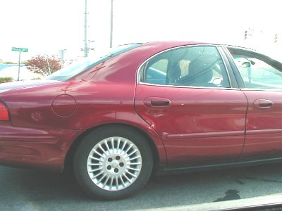 1997 Ford Taurus - Side view of a red sedan, likely from the 2000 model year based on its body style.