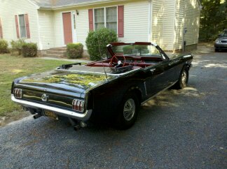 1965 Ford Mustang - Rear view of a black convertible classic car parked on a gravel driveway.