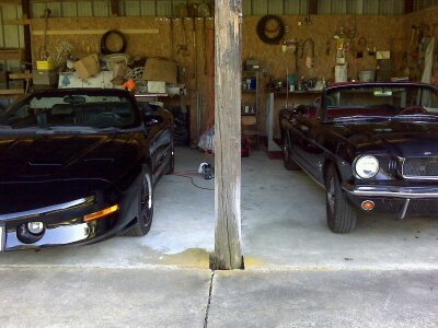 1965 Ford Mustang - A 1965 Ford Mustang convertible is parked in a garage alongside another black convertible.