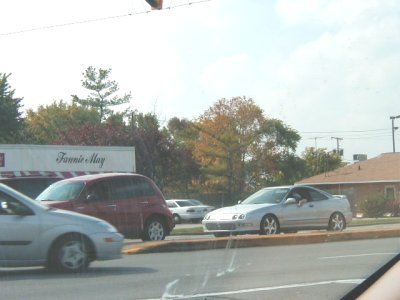 1997 Ford Taurus - Several vehicles are visible on a street with trees and buildings in the background under a cloudy sky.