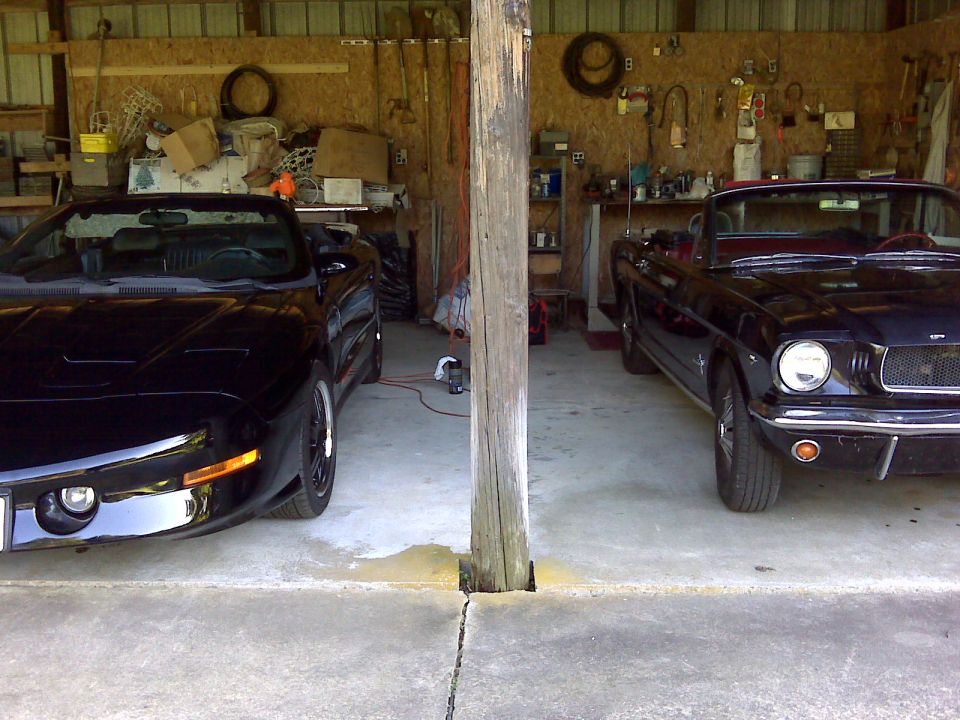 Two black convertible sports cars parked in a garage: a Pontiac Firebird and a classic Ford Mustang.