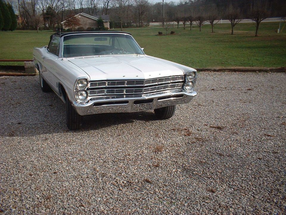 White convertible parked on gravel lot, front end visible