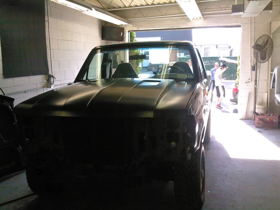 Front view of a dark-colored Ford truck in a garage, hood scoop visible