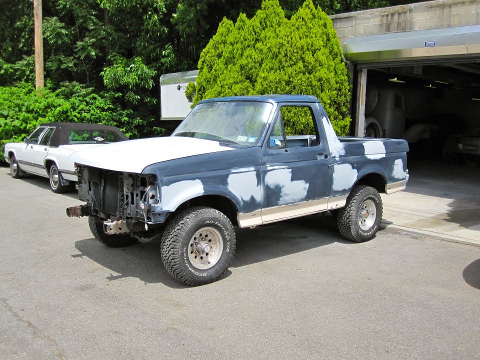 1992 Ford Bronco with primer patches on body, hood is white, front grille missing