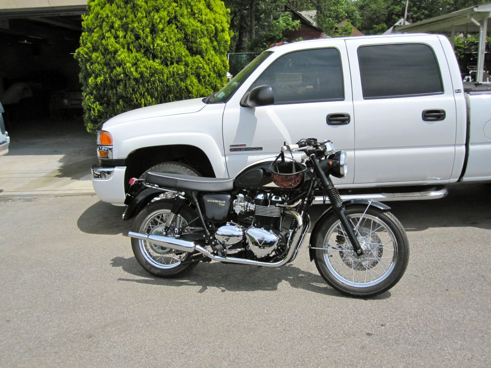 Black Triumph Bonneville T100 motorcycle parked in a driveway in front of a white GMC pickup truck