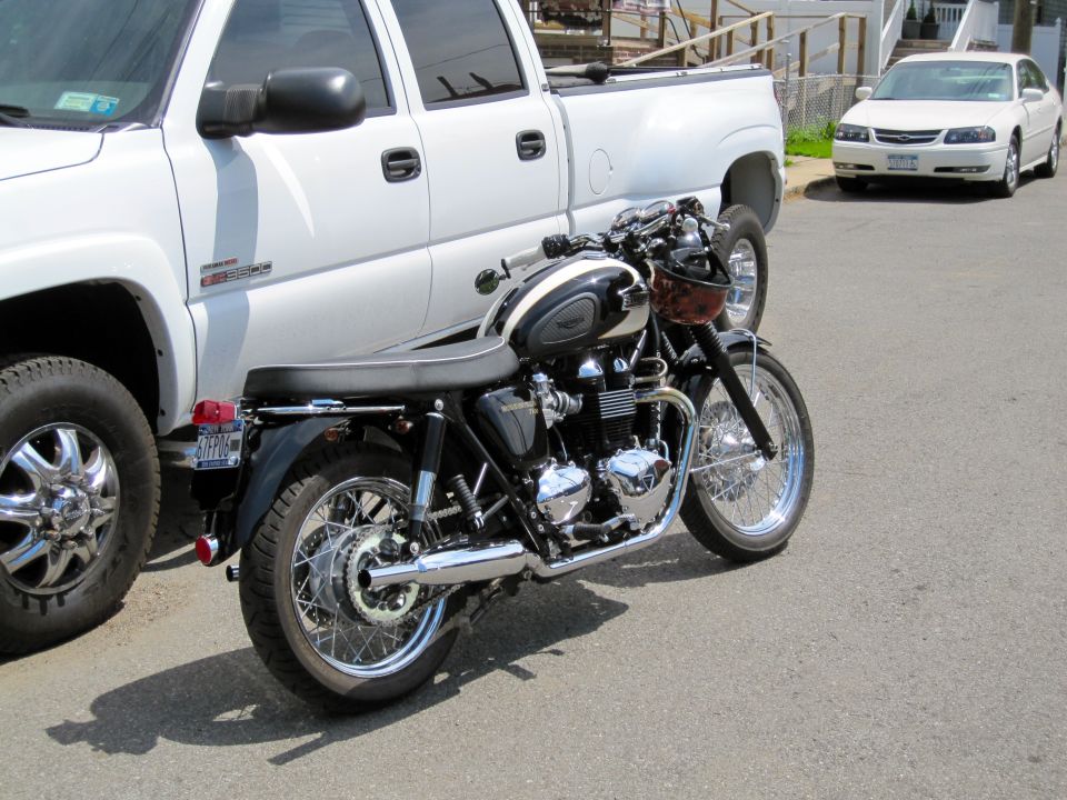 Black and white motorcycle parked next to a white pickup truck, with a white sedan in the background