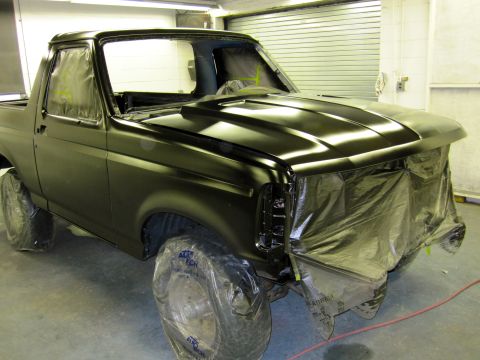 1992 Ford Bronco - A black SUV is being prepped for painting in a workshop, with its wheels covered and the front end masked off.