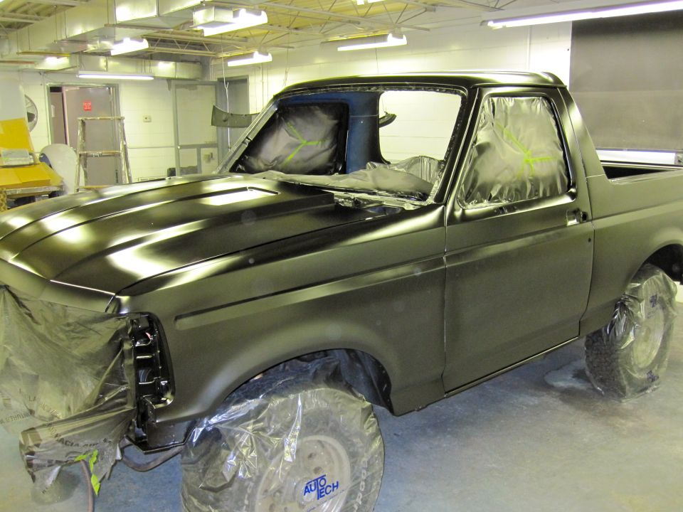 1992 Ford Bronco covered in plastic and primer in a paint booth