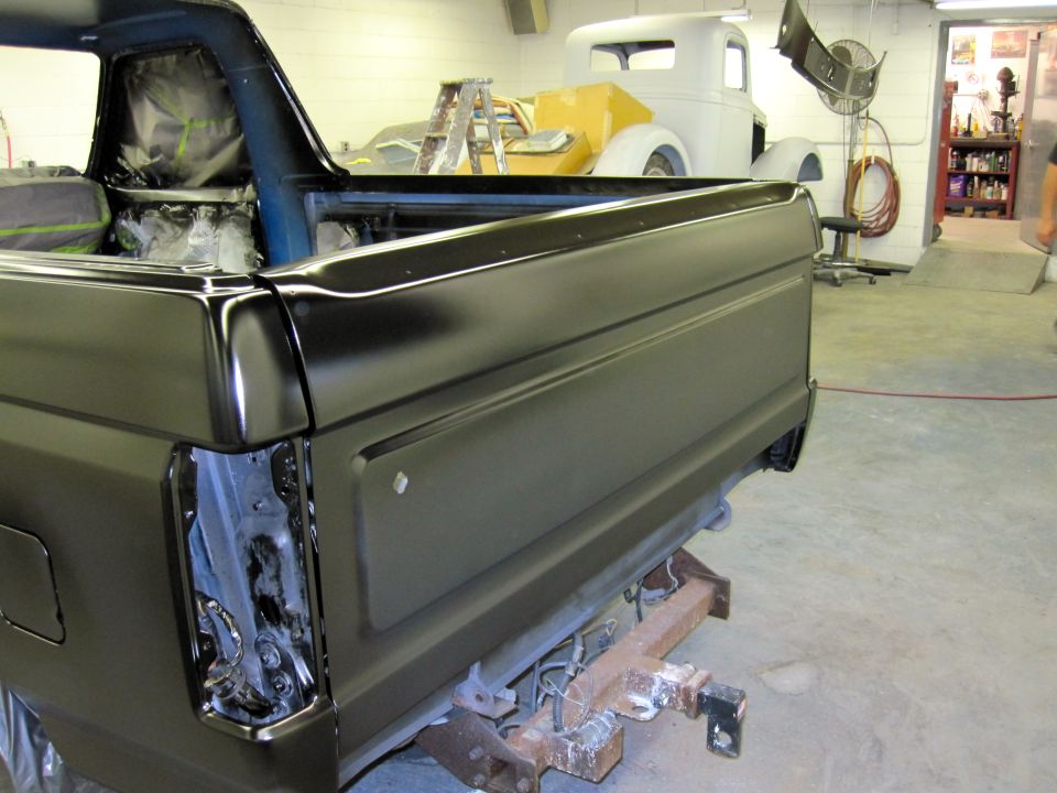 Black Ford Bronco rear quarter panel with blue interior visible, in a workshop with another vehicle