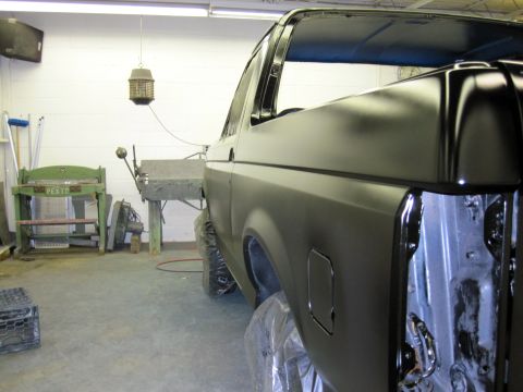 1992 Ford Bronco - A black SUV is seen in a workshop, with its rear quarter panel and wheels covered in plastic sheeting.