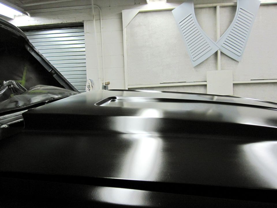 Black car hood with a raised scoop, showing reflections. Garage door in background