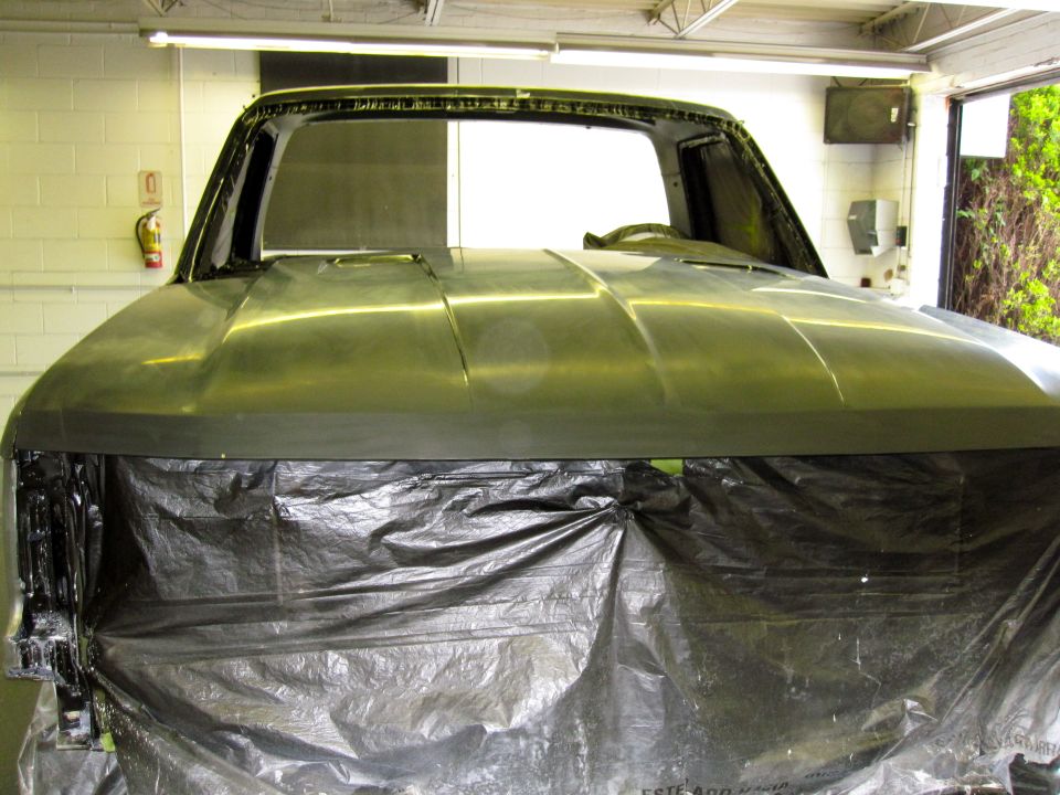 Unfinished Ford Bronco body, front view, covered in black plastic sheeting, showing the hood and windshield frame