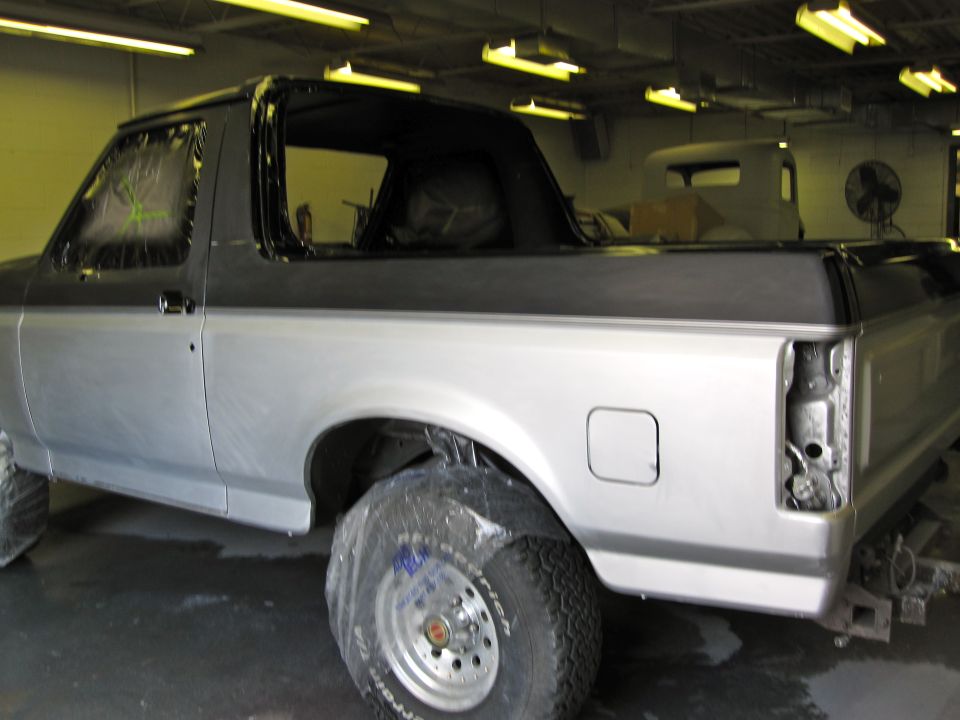 1992 Ford Bronco in a shop, prepped for paint with plastic on wheels