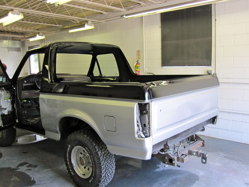 Silver and black 1992 Ford Bronco in a garage, rear quarter view, with doors open and interior visible