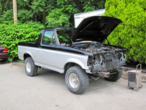 1992 Ford Bronco - A two-tone black and silver 1992 Ford Bronco is parked outside with its hood open and the front grille missing.