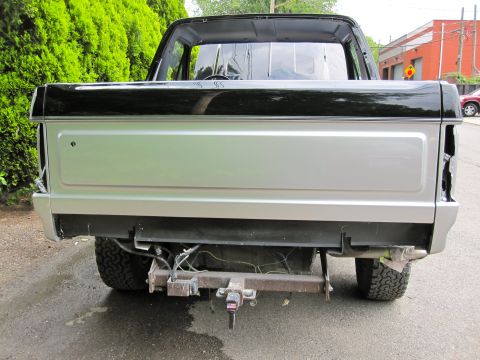 1992 Ford Bronco - The rear view of a silver pickup truck with a black bed rail and cab top is shown. The truck has a visible trailer hitch and exposed wiring…