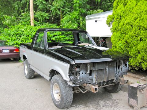 1992 Ford Bronco - A two-tone black and silver Ford Bronco is parked outdoors with its front end disassembled, revealing the radiator and engine components. A…