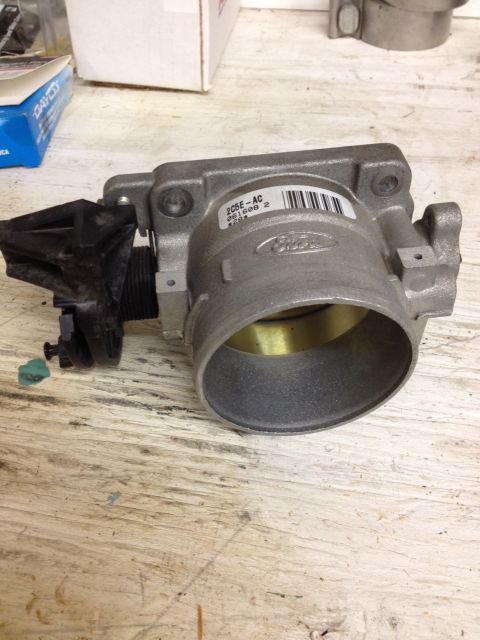 1998 Ford Crown Victoria - A Ford throttle body is shown with a visible part number and barcode on a wooden surface.