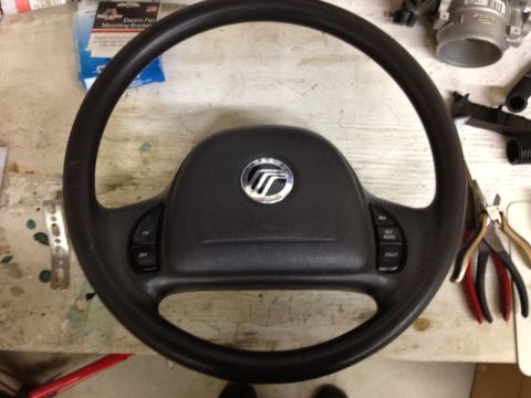 1998 Ford Crown Victoria - Steering wheel the Mercury emblem and cruise control buttons, likely from a Mercury vehicle.