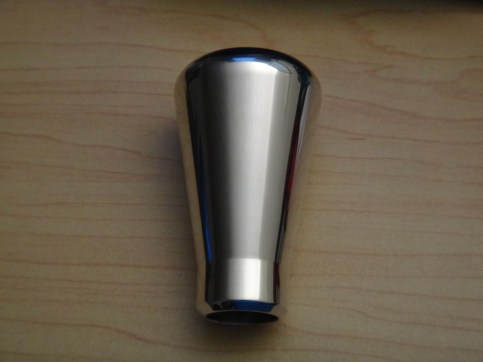 Polished chrome shift knob with a tapered shape, resting on a wood-grain surface