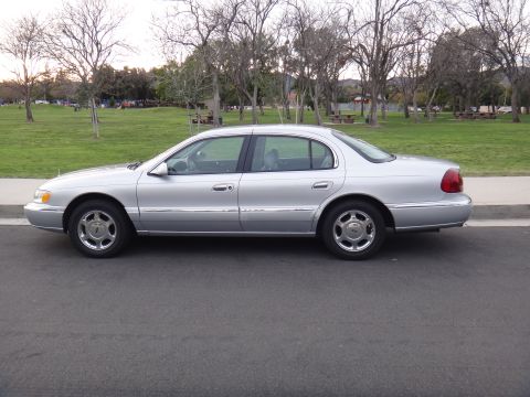 2000 Lincoln Continental - A silver 2000 Lincoln Continental sedan is parked on the side of the road with a park in the background.