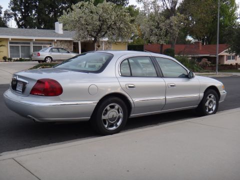 2000 Lincoln Continental - A silver sedan is parked on the side of a residential street with houses and trees in the background.