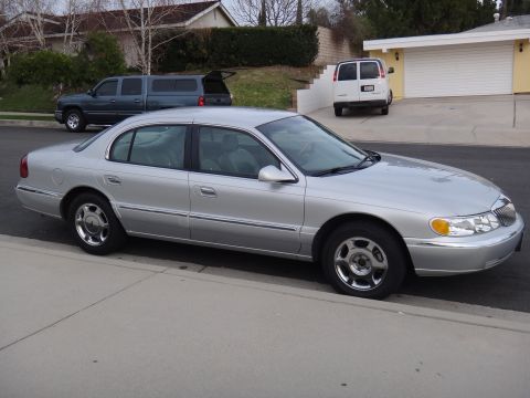 2000 Lincoln Continental - Silver 2000 Lincoln Continental parked curbside with other vehicles in the driveway behind.