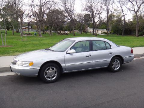 2000 Lincoln Continental - A silver sedan is parked on the side of the road with a park in the background.