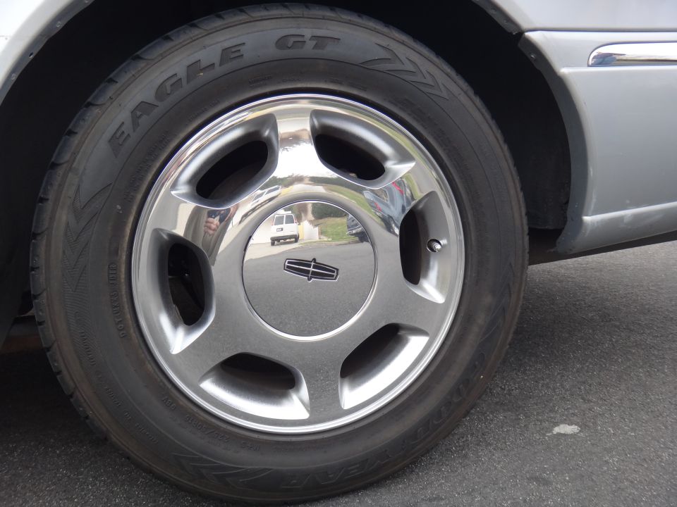 Silver Lincoln Continental wheel with a Lincoln emblem and Eagle GT tire. Reflection shows a white van