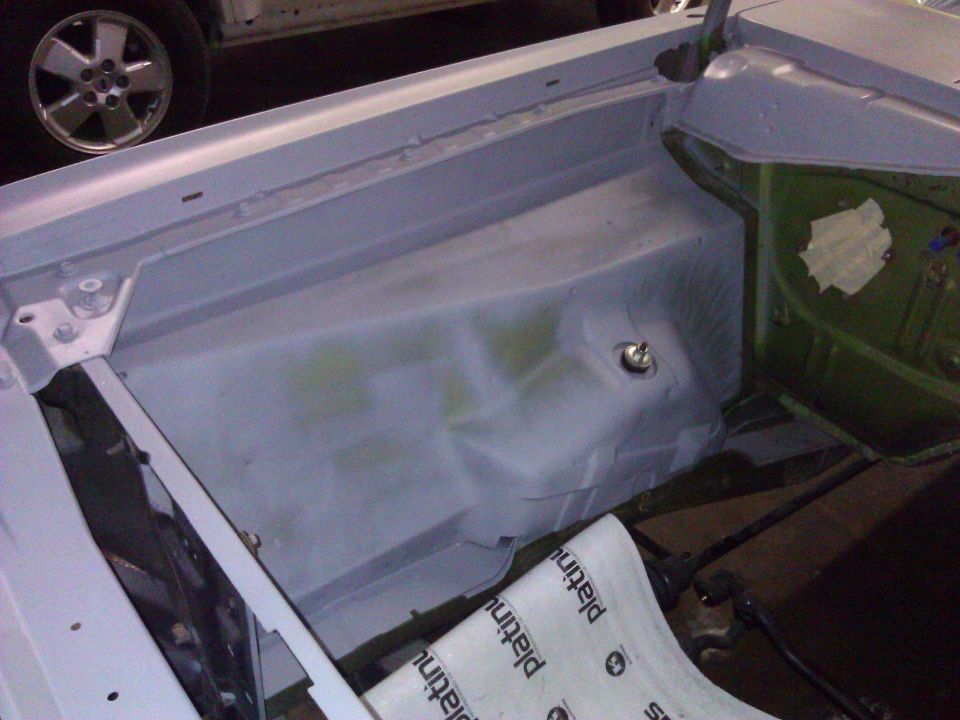 Car's inner fender well area, primed, with a wheel and part of another vehicle visible