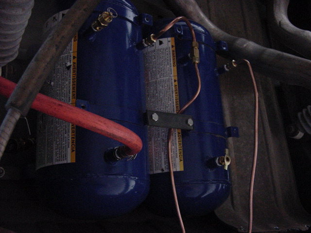 Two blue air tanks with brass fittings and copper lines mounted under vehicle chassis