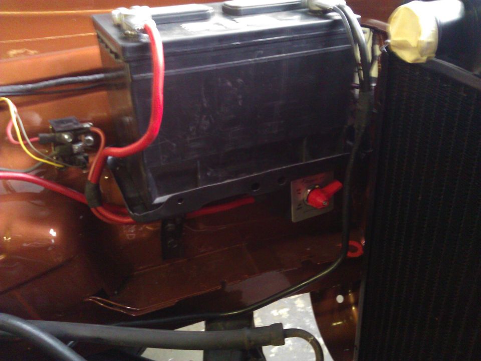 Car battery with red cables and a red kill switch mounted nearby