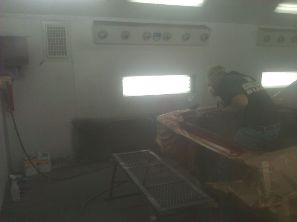 Car body covered in plastic sheeting inside a spray booth with a person painting