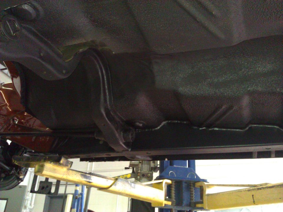 Underside of a car on a lift, showing the fuel tank and frame rails