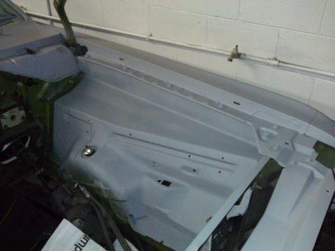1971 Dodge Dart - The engine bay of a car is shown, prepped with primer, revealing the inner fender and hood hinge structure.