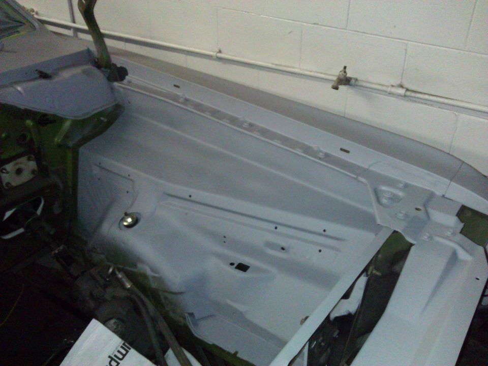 Car engine bay primed for restoration, showing inner fender and hood hinge area
