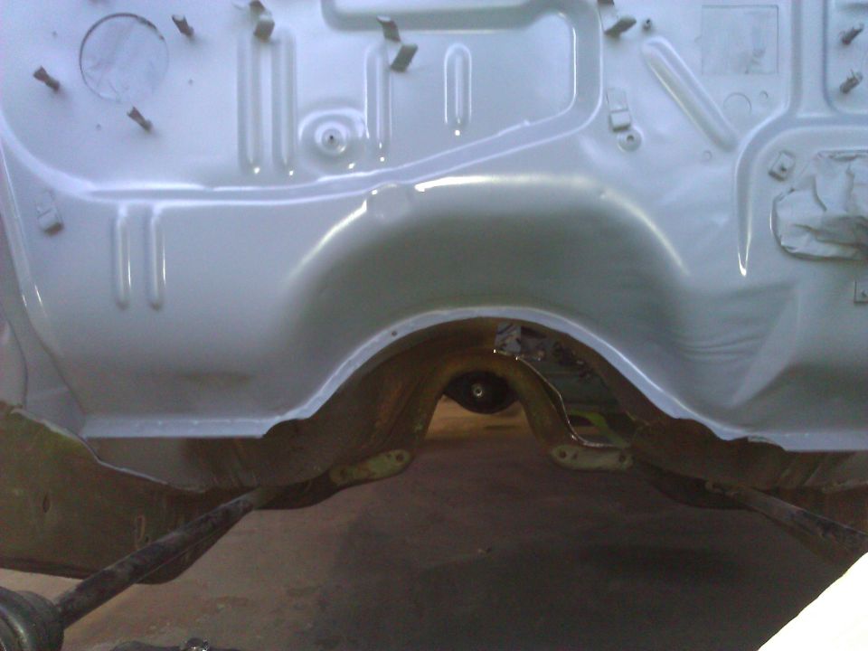Car chassis with suspension components and wheel well visible, painted light gray
