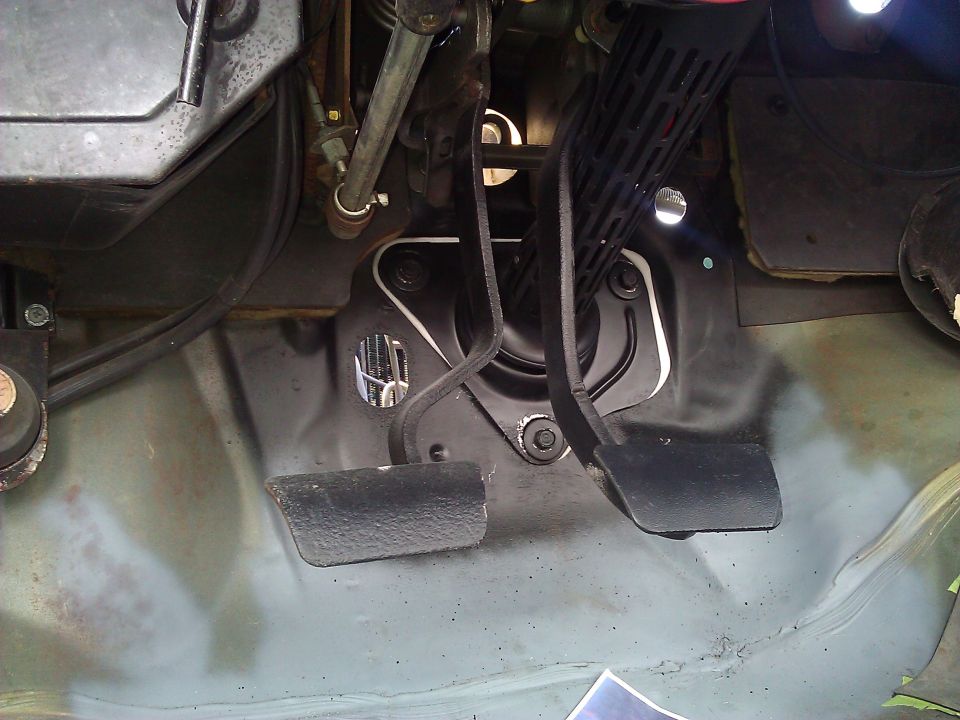 Car interior showing brake and accelerator pedals, with linkage visible above